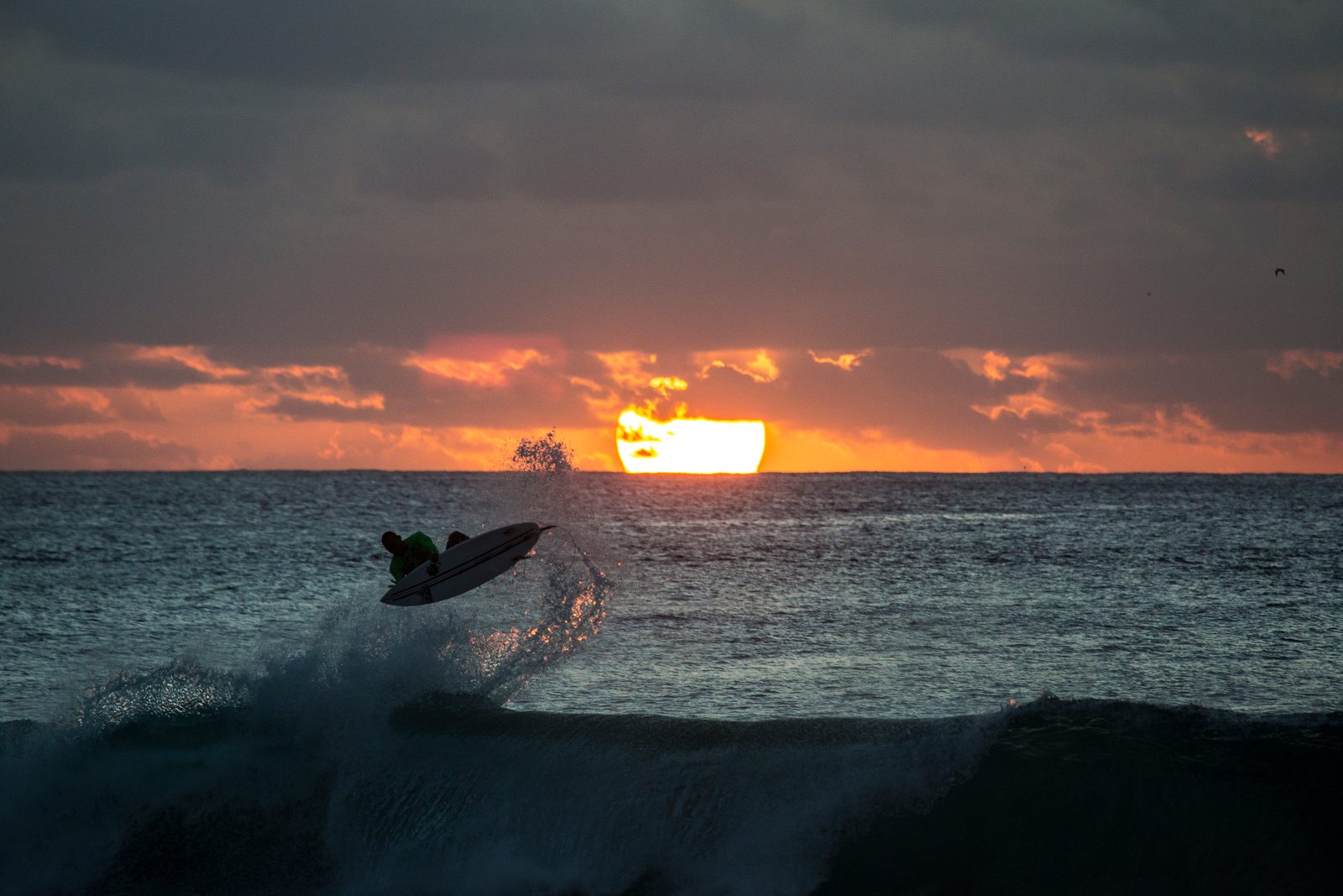 Breaking ocean wave beneath a setting sun