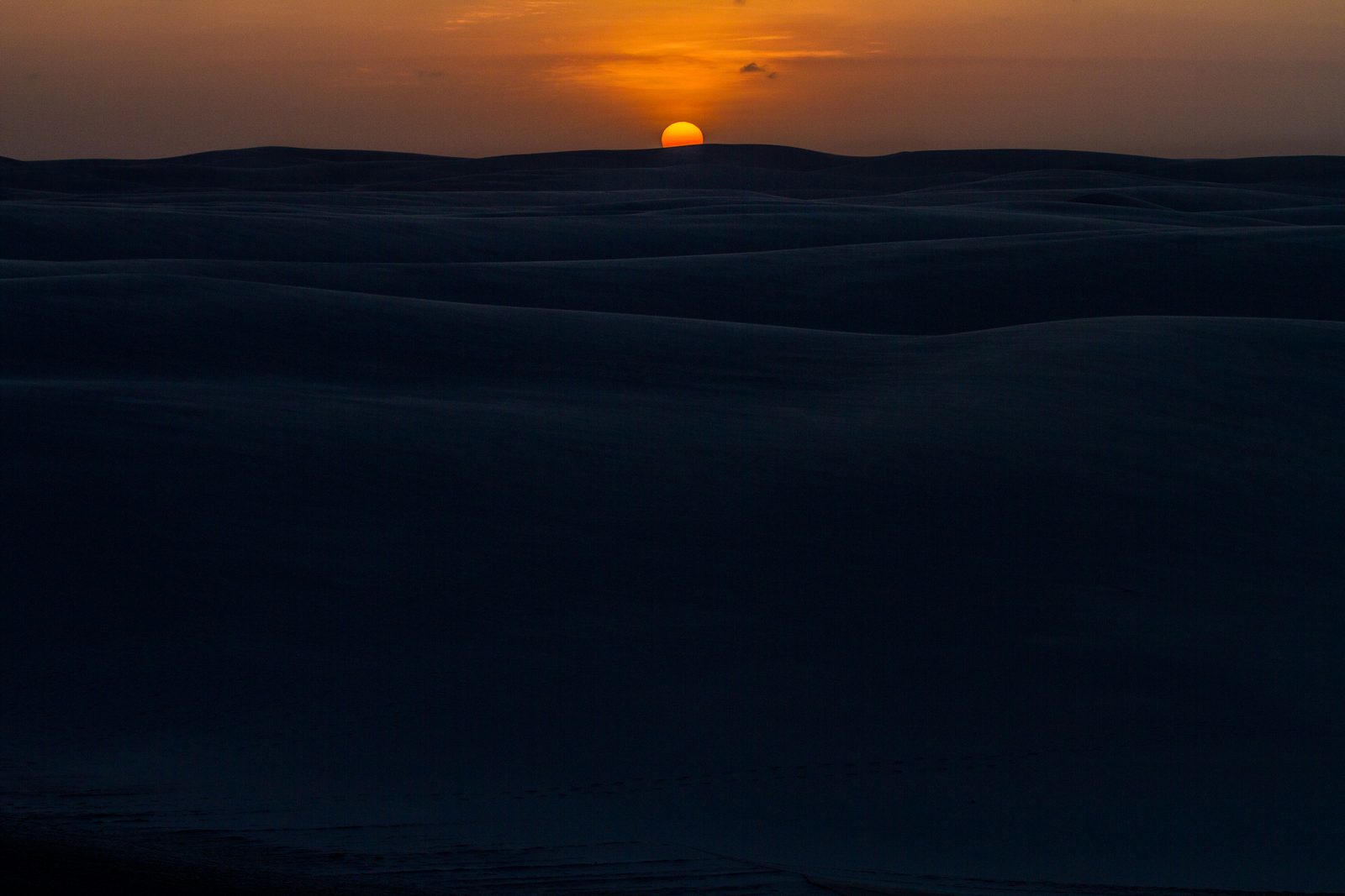 Orange sun setting above dark dunes